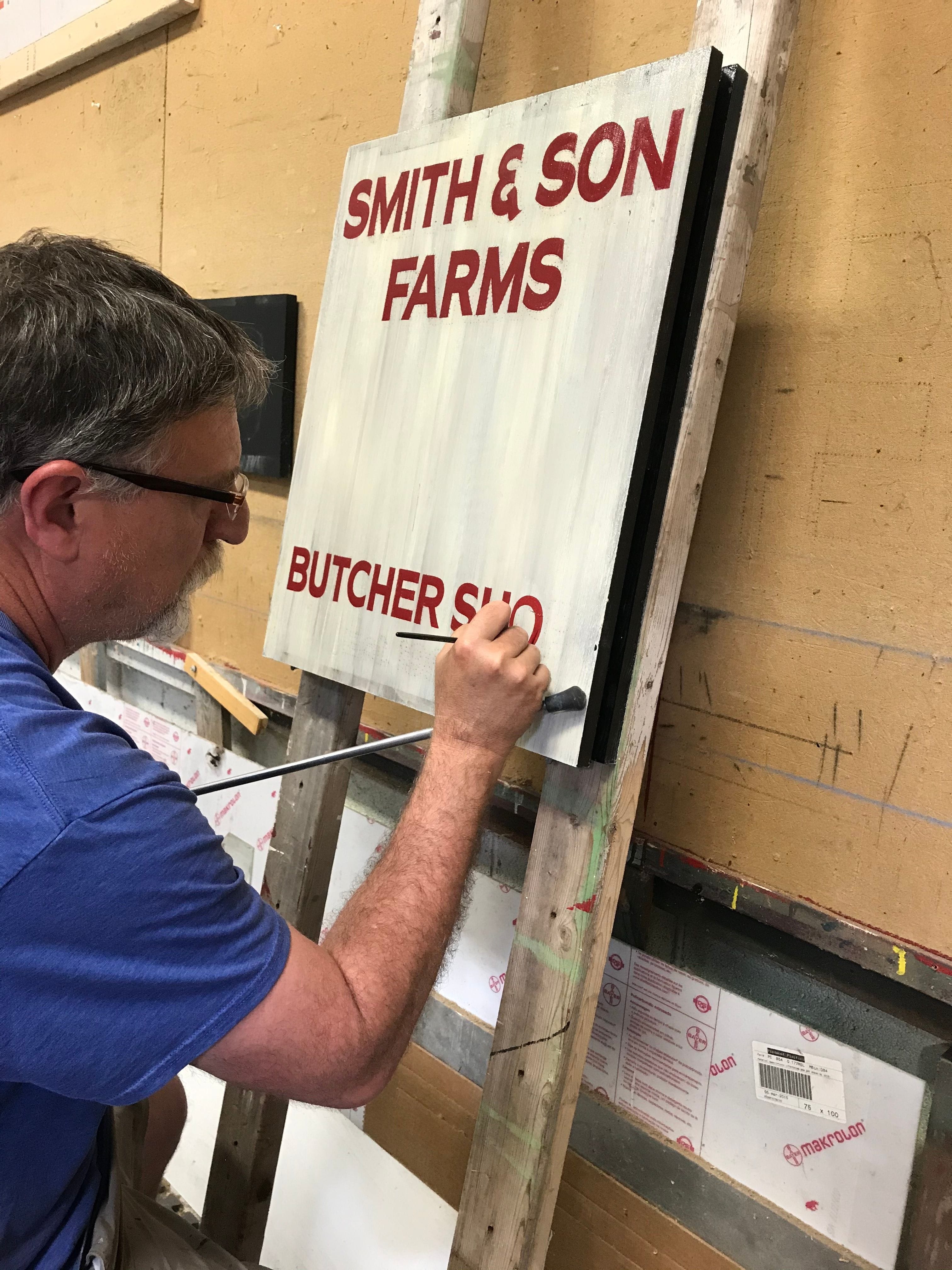 Tim is hand lettering an interior sign for a restaurant. It is being painted to look rustic and worn.